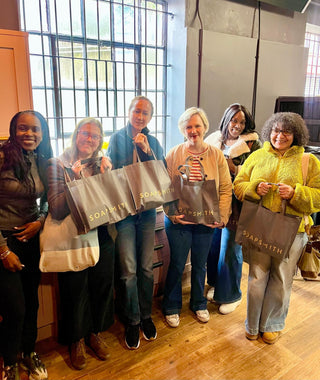 A group of Soapsmith workshop guests holding their tote bags in the studio