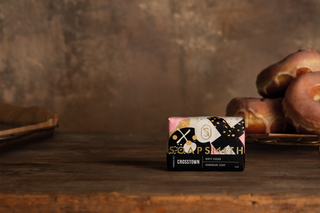 Soapsmith x Crosstown Dirty Sugar soap with its complete black, gold and pink wrapper beside glazed doughnuts.